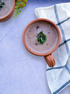 An earthen cup containing ragi soup and a tempering of cumin seeds and curry leaves.