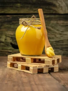 Jar of clarified ghee on rustic table with spoon.